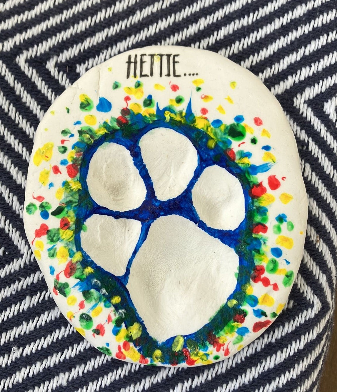 Paw print painted in a colourful splattered dot effect with the name Hettie at the top