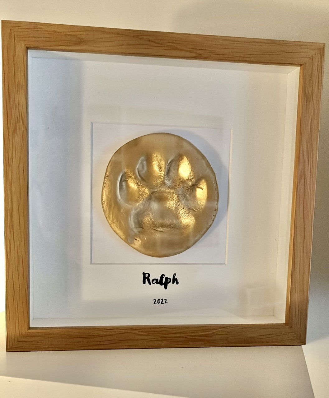 finished paw print painted gold in a box frame with the name Ralph underneath and the year 2022